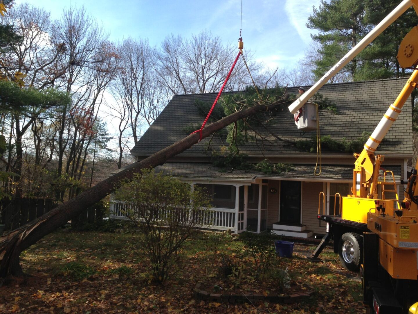 A crane is being used to remove a tree from the roof of a house.