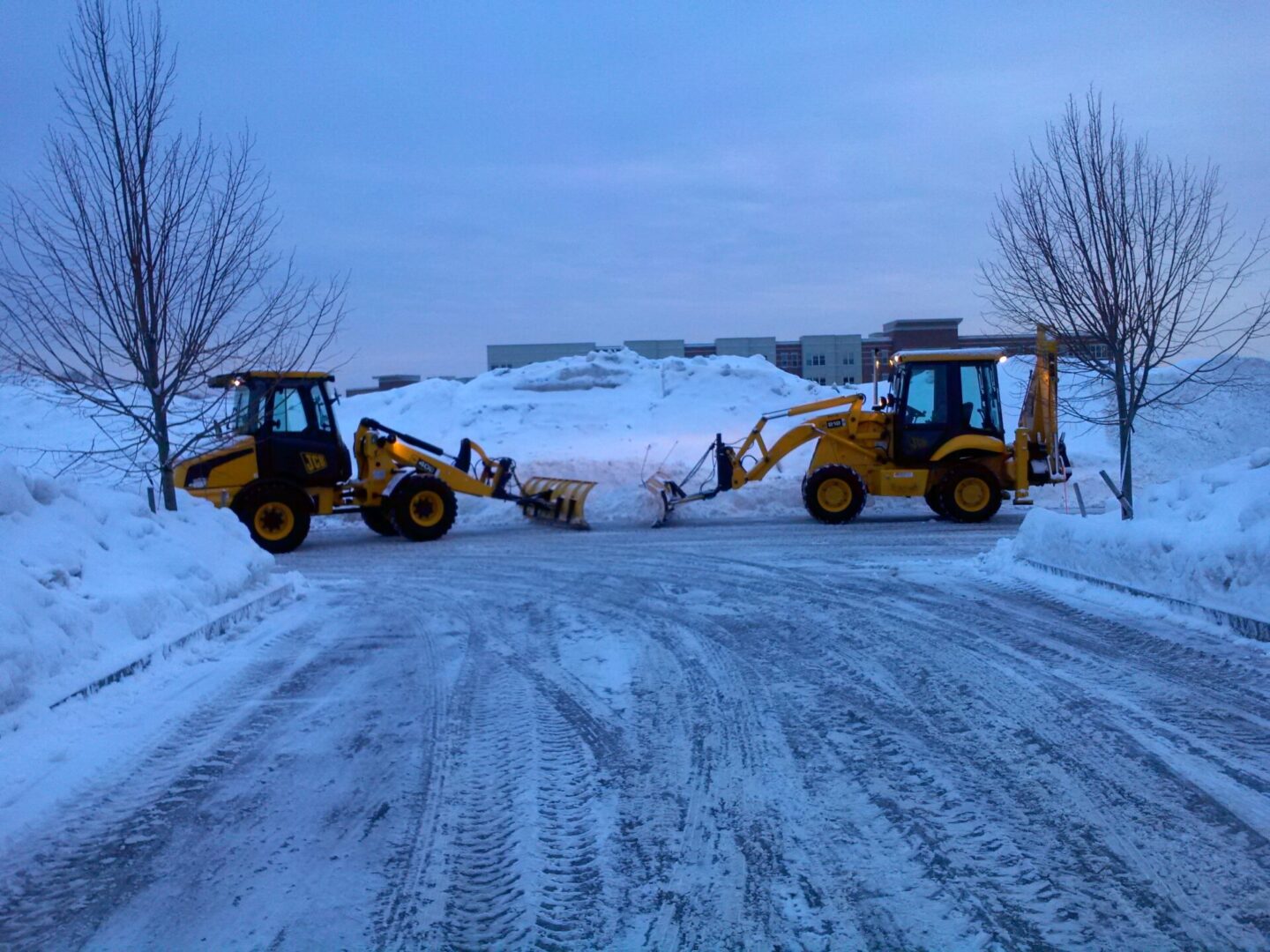 Two backhoes are parked on a snowy road.